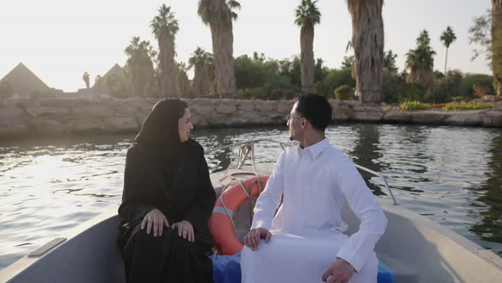 Spending enjoyable time outdoors, conversations and discussions in natural surroundings, gestures of happiness and joy, an Arab Gulf Saudi man wearing a white thobe sitting outdoors on a boat with his wife.