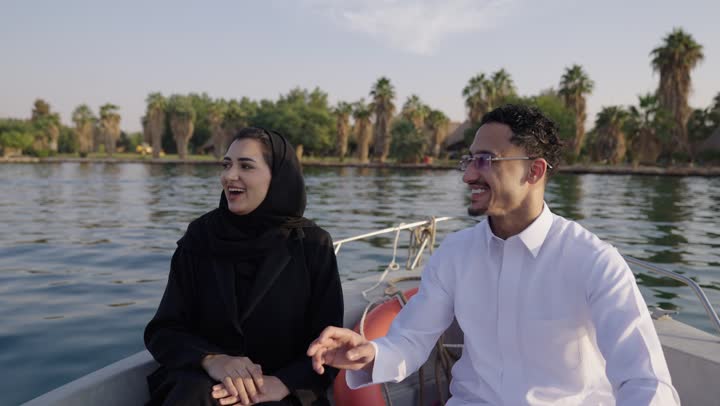 حوارات ونقاشات في الأجواء الطبيعية،ايماءات السعادة و السرور، رجل عربي خليجي سعودي يرتدي الثوب الابيض يجلس فى الهواء الطلق على مركب برفقة زوجته ، قضاء وقت ممتع فى الخارج