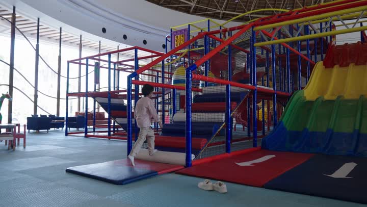 The beginning of a journey of fun and entertainment in the amusement park, a small Arab Saudi Gulf boy wearing casual attire climbs the steps of the colorful foam ladder in preparation for riding the slide, moments filled with anticipation and excitement, enjoying the amusement park.
