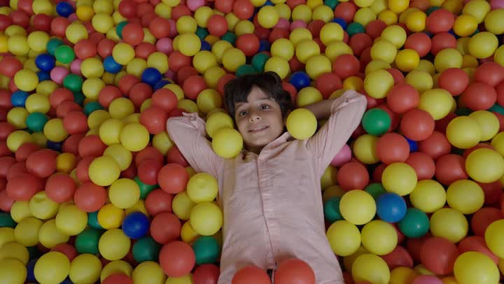 اخذ استراحة قصيرة من اللعب و اللهو في مدينة الملاهي , ولد عربي خليجي سعودي صغير ينام بين الكرات الصغيرة الملونة ,لحظة مليئة بالراحة والسلام مع ايماءات السعادة و الابتسام , الاستمتاع باللعب في مدينة الملاهي