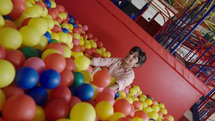 اللعب بمرح في بيت الكرات ,ولد صغير عربي سعودي خليجي يرتدي الزي الكاجوال يقذف الكرات الصغيرة لاعلى ومشاهدتها تسقط في سعادة ,لحظات مليئة بالبهجة و السرور