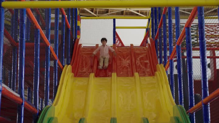 الابتسام و ايماءات السعادة اثناء التزلج بسرعة للاسفل على الزحلوقة ,طفل عربي خليجي سعودي يرتدي الزي الكاجوال يقضي أوقات ممتعة لا تنسى في مدينة الملاهي , الاستمتاع باللعب في مدينة الملاهي