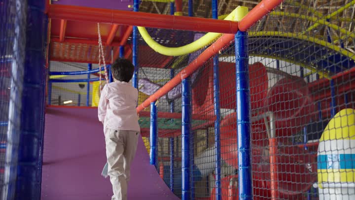 التقاط الانفاس بعد الوصول للقمة ,طفل عربي سعودي خليجي يرتدي الزي الكاجوال يتسلق على الحبل ليصل للاعلى , مفهوم تعلم الاصرار مع اللهو و اللعب , الاستمتاع باللعب في مدينة الملاهي