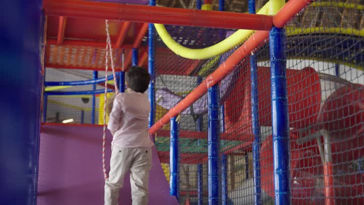 طفل عربي سعودي خليجي يرتدي الزي الكاجوال يتسلق الحبال ,مدينة ملاهي أمنة للحفاظ على سلامة الاطفال ,اشارات الانتصار عند الوصول للقمة ,ايماءات السعادة والسرور , الاستمتاع باللعب في مدينة الملاهي