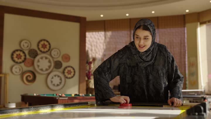 Engaging in recreational activities and events within a unique family framework, an Arab Gulf Saudi girl wearing a gray abaya, cheering and smiling after scoring a goal and achieving victory.