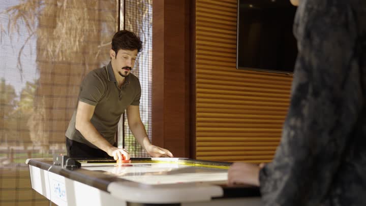 شاب عربي خليجي سعودي يرتدي الزي الكاجوال يقضي وقت ممتع مع امه ,لعبة الهوكي الهوائي من الالعاب الجماعية المميزة ,انشطة ترفيهية في جو من السعادة و السرور