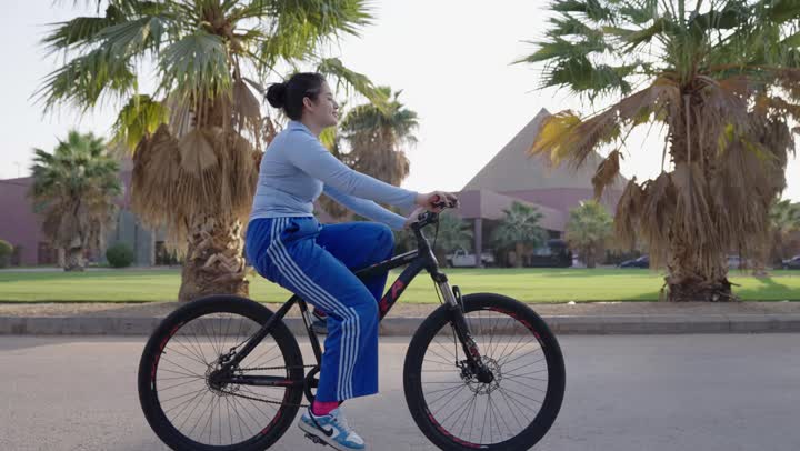 النظر باتجاه الشمس الساطعة اثناء ركوب الدراجة الهوائية ,الشعور بالهواء الدافئ , فتاة عربية خليجية سعودية ترتدي الزي الكاجوال