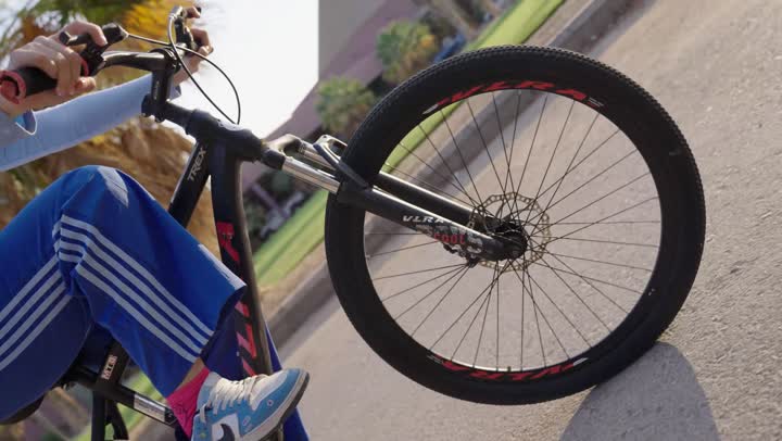 اطار الدراجة الهوائية يدور في دوائر لانهائية ,فتاة عربية خليجية سعودية تقوم بلف الاطارات باحترافية , رؤية انعكاس الدراجة على الطريق في وقت الظهيرة