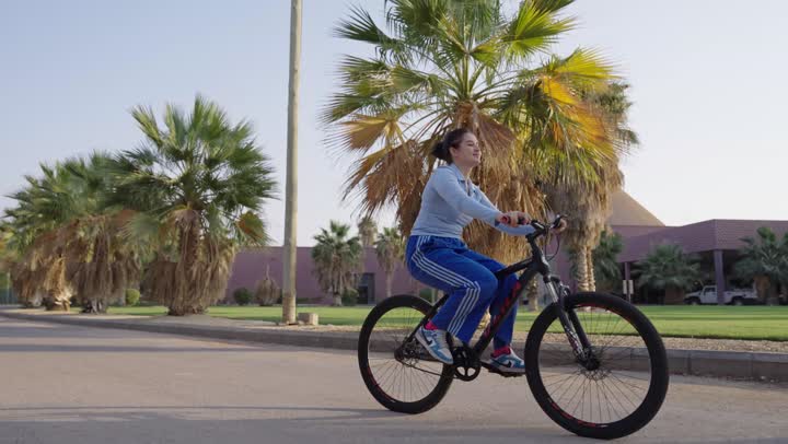 فتاة عربية خليجية سعودية ترتدي الزي الكاجوال تركب الدراجة الهوائية بين النباتات و الحشائش ,الاستمتاع بالجو الدافئ و السماء الصافية ,