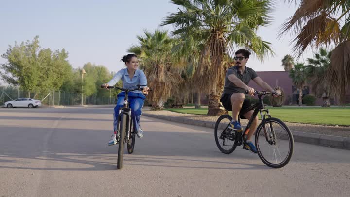 حديث عائلي شيق بين الاخوة ,جولة داخل المجمع السكني بالدراجة الهوائية ,شاب عربي سعودي خليجي يرتدي الزي الكاجوال و النظارة الشمسية ,فتاة عربية خليجية سعودية ترتدي السروال الازرق ,مشاهد تعكس الطبيعة الخلابة