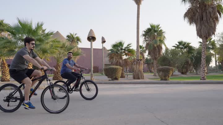 The father and son are on a family bike ride, the warm and mild weather among the trees and enchanting nature, two Arab Gulf men from Saudi Arabia wearing casual attire.