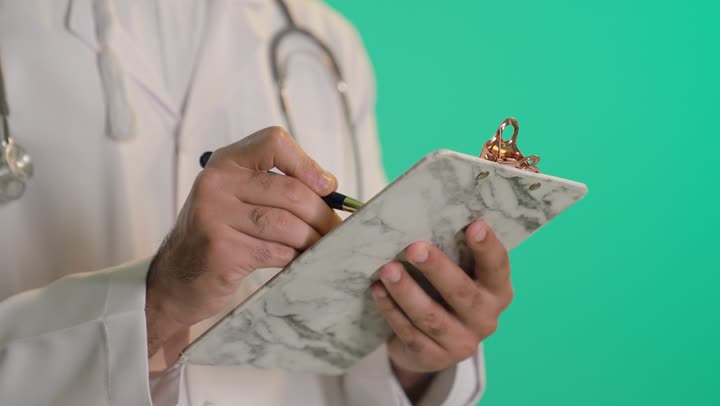 تدوين الملاحظات والبيانات، العمل في المراكز والمستشفيات، الطب والرعاية الصحية، بورتريه مقرب ليد طبيب عربي خليجي عماني يقوم بالكتابة، خلفية خضراء ، كروما