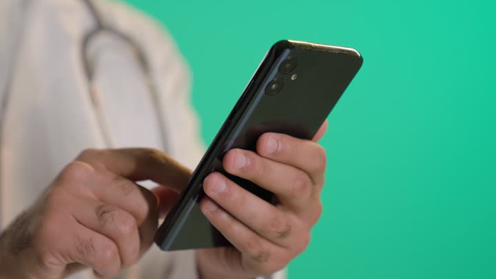 تقديم الخدمات العلاجية، استخدام التقنية الحديثه في المجال الطبي, بورتريه مقرب ليد لطبيب عربي خليجي عماني يضع السماعة الطبية يستخدم الهاتف المحمول ، خلفية خضراء ، كروما