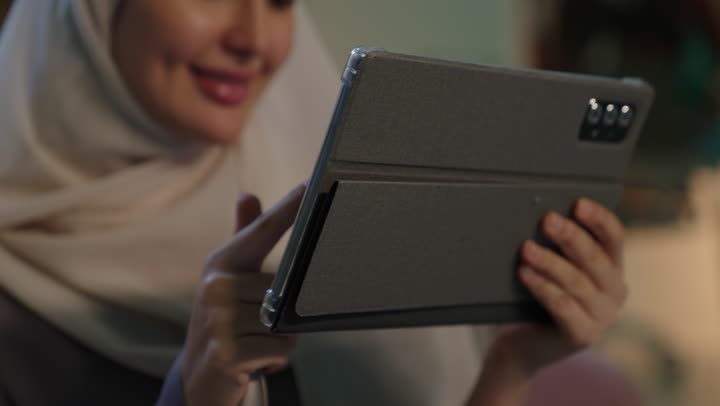 التسوق الالكتروني عبر الأونلاين، استخدام وسائل تقنية حديثة ومتطورة، إنجاز المهام عن بعد، التطبيقات التقنية للأجهزة اللوحية،تصوير مقرب  لشابة عربية خليجية سعودية محجبة ترتدي العباءة تقوم بإنجاز مهام العمل عبر جهاز التابلت