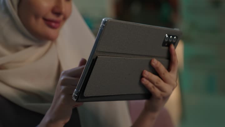 استخدام وسائل تقنية حديثة ومتطورة، إنجاز المهام عن بعد، التسوق الالكتروني عبر الأونلاين، التطبيقات التقنية للأجهزة اللوحية،تصوير مقرب  لشابة عربية خليجية سعودية محجبة ترتدي العباءة تقوم بإنجاز مهام العمل عبر جهاز التابلت