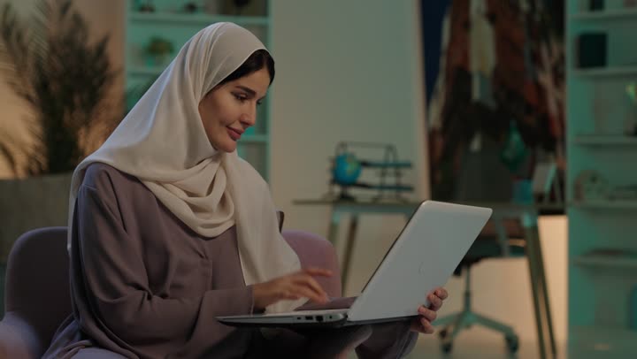 مفهوم ادخال البيانات، دمج التكنولوجيا الحديثة بالحياة العملية، النقر على لوحة المفاتيح، صناعة المحتويات النصية، شابة عربية خليجية سعودية ترتدي العباءة و الحجاب تستخدم الحاسوب المحمول، الكتابة على جهازاللابتوب