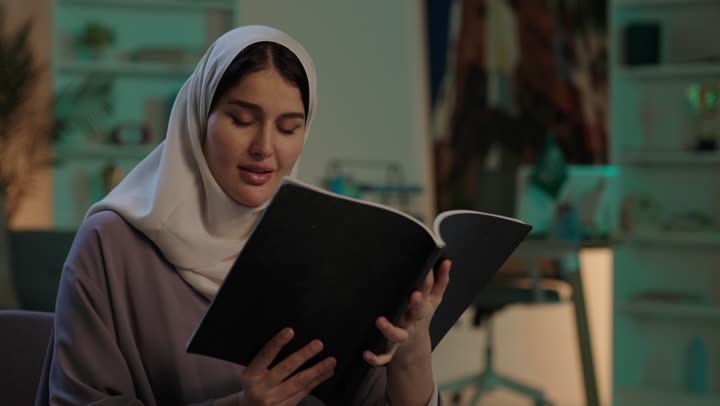 Developing skills and expanding knowledge and ideas, enjoying reading books, stories, and novels, a young Arab Gulf Saudi woman wearing an abaya and hijab holding a book in her hands, increasing intellectual resources, spending free time in a beneficial way.
