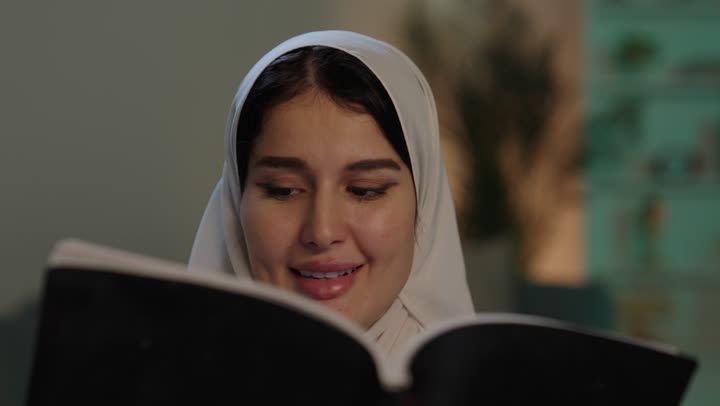 الاستمتاع بقراءة الروايات والقصص، قراءة الكتب بتمعن، ثقافة التعلم الذاتي، تصوير مقرب لشابة عربية خليجية سعودية ترتدي العباءة والحجاب تحمل بيدها كتاب تثقيفي ، إيماءات التركيز والاندماج