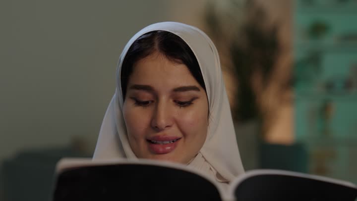 The culture of self-learning, reading books attentively, a close-up shot of a young Arab Gulf Saudi woman wearing an abaya and hijab holding an educational book in her hand, gestures of focus and engagement, enjoying reading novels and stories.