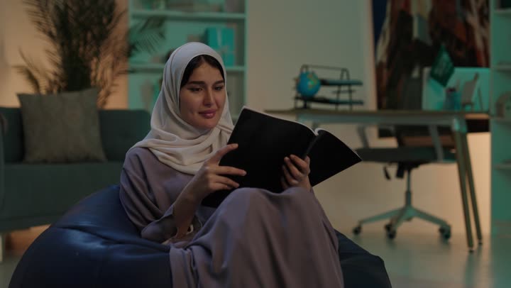 قضاء الوقت بالتعلم والتثقف، مفهوم الشغف بالمطالعة، الاستمتاع بقراءة الكتب والقصص والروايات، شابة عربية خليجية سعودية ترتدي العباءة و الحجاب تجلس على كرسي بين باج تحمل بيديها كتاب، ثقافة التعلم الذاتي