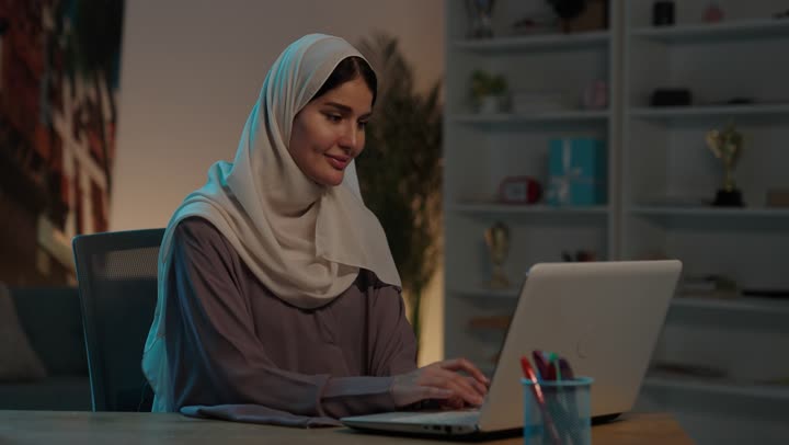 إدارة الأعمال عن بعد, شابة عربية خليجية سعودية ترتدي العباءة و الحجاب تقوم  بانجاز المهام عبر الحاسب المحمول, استخدام الأجهزة والتقنيات الحديثة