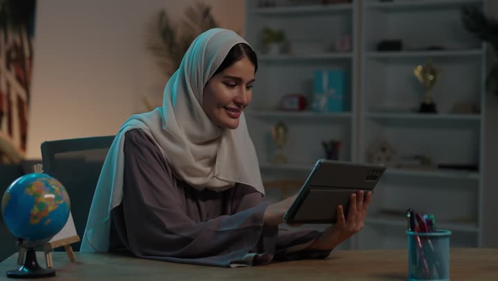 تصفح مواقع و وسائل التواصل الاجتماعي، دمج التقنية في الحياة اليومية والعملية، شابة عربية خليجية سعودية ترتدي العباءة والحجاب تقوم بانجاز مهام العمل عبر جهاز التابلت، استخدام الاجهزة التقنية الحديثة ، مفهوم انجار المشاريع عن بعد