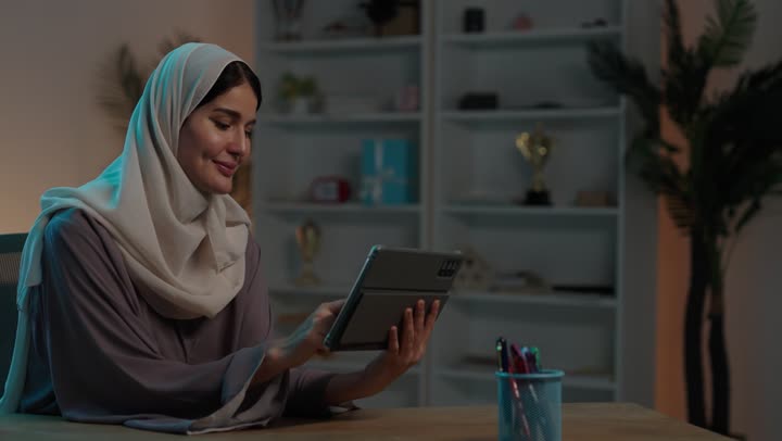 تصفح مواقع ووسائل التواصل الاجتماعي، دمج التقنية والتكنولوجيا الحديثة في الحياة اليومية،  شابة عربية خليجية سعودية محجبة ترتدي العباءة تقوم بالنقر على جهاز التابلت، ايماءات السعادة و السرور