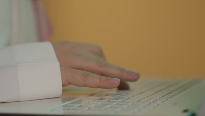 Typing on the keyboard, a close-up portrait of the hand of a Saudi Arabian Gulf man using a laptop, the concept of remote work, brown background.