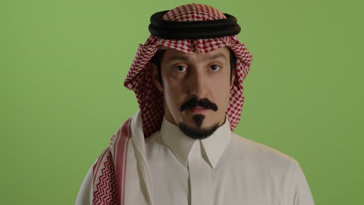 الهدوء والسكون وعدم الإزعاج، التوقف عن الكلام وخفض الصوت، بورتريه مقرب لرجل عربي خليجي سعودي يرتدي الثوب الابيض والشماغ يضع أصبع السبابة على فمه، طلب السكوت والصمت، حركة أصبع وإشارات، خلفية خضراء