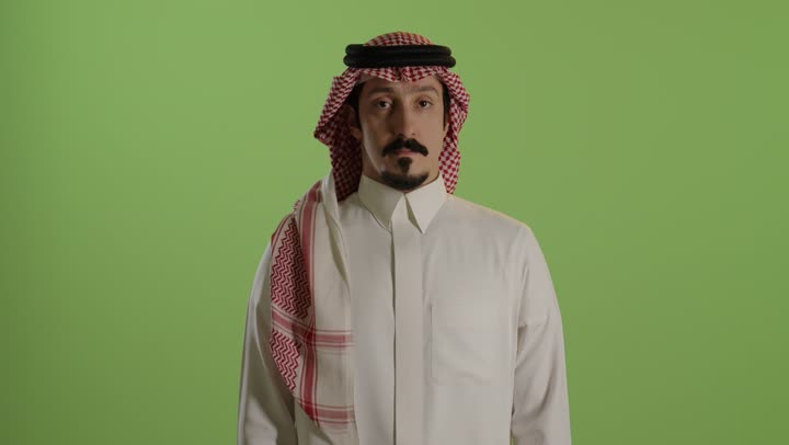طلب التوقف وعدم الاقتراب، مفهوم الرفض والامتناع والانزعاج, بورتريه لرجل عربي خليجي سعودي يرتدي الثوب الابيض والشماغ يمد يده نحو الأمام مع رفع الكف بإيماءات النهي عن فعل امر ما, تعابير الحزم والجدية, خلفية خضراء