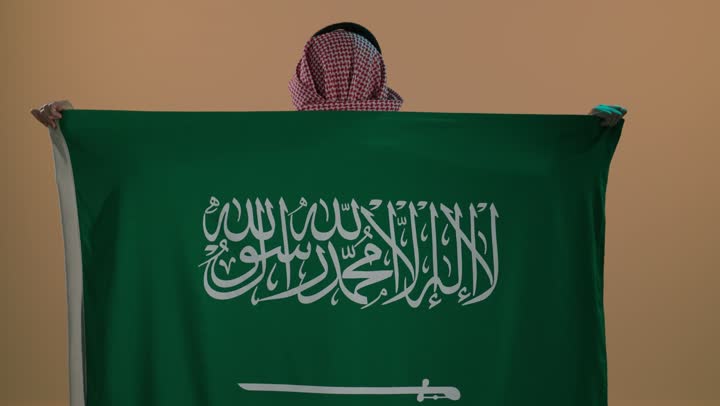الفخر والاعتزاز بإنجازات الوطن، شعار الهوية الوطنية وراية الإسلام والتوحيد، بورتريه لرجل عربي خليجي سعودي يرتدي الثوب و الشماغ يضع علم التأسيس على كتفية , ذكرى تأسيس الدولة السعودية الأولى 22 فبراير، خلفية بنية