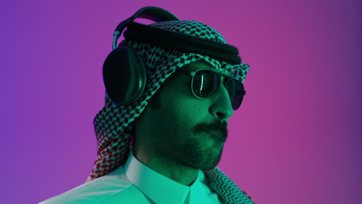مفهوم الرقص والتفاعل مع الموسيقى، بورتريه مقرب لشاب عربي خليجي سعودي يرتدي الثوب الابيض و الشماغ و النظارة الشمسية يستمتع بسماع الأغاني المتنوعة، الشعور بالفرح والسعادة والسرور، خلفية ملونه