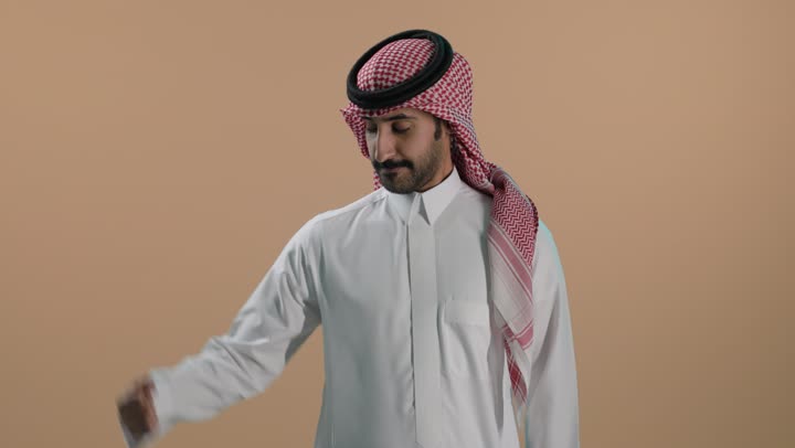 التمتع بالبنية الجسدية القوية، ورتريه لشاب عربي خليجي سعودي يرتدي الثوب الابيض والشماغ ويقوم بعرض عضلات يديه، إيماءات وجه ويدين تدل على القوة العضلية، اللياقة البدنية والجسم الصحي المتين، خلفية بنية