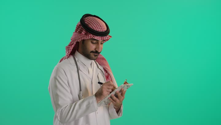 الطب والرعاية الصحية، التفكير و محاولة تذكر شيء ، العمل في المراكز والمستشفيات، تدوين الملاحظات والبيانات، بورتريه لطبيب عربي خليجي سعودي يرتدي الشماغ و المعطف الطبي الأبيض يضع سماعة الفحص الطبية يقوم بالكتابة، خلفية خضراء ، كروما