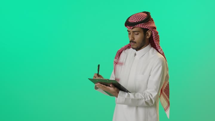 تسجيل الملاحظات والمعلومات، إدارة الأعمال وتنظيمها, بورترية لشاب عربي خليجي سعودي يرتدي الثوب الابيض و الشماغ يقوم بكتابة المهام والأهداف اليومية، خلفية خضراء ، كروما