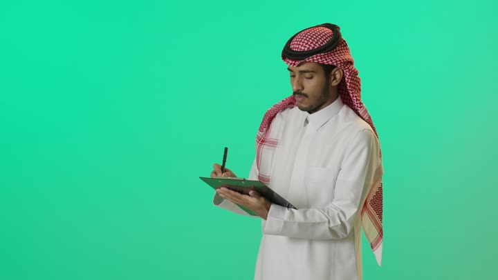تدوين وتسجيل البيانات، إدارة الأعمال وتنظيمها, بورترية لشاب عربي خليجي سعودي يرتدي الثوب الابيض و الشماغ يقوم بكتابة المهام والأهداف اليومية، خلفية خضراء ، كروما