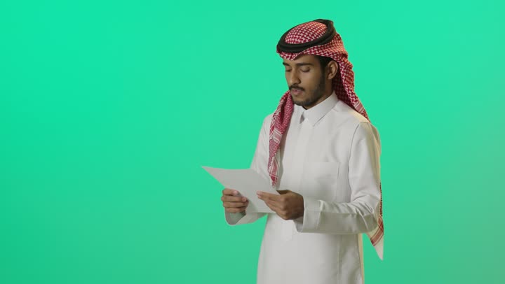 مراجعة ومتابعة الخطط والمشاريع المكتبية، اعداد التقارير الخاصة بالعمل، بورترية لشاب عربي خليجي سعودي يرتدي الثوب الابيض و الشماغ يحمل بيده مجموعة من الاوراق، التدقيق في قراءة الملاحظات، خلفية خضراء، كروما