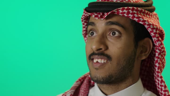 Searching for something, the concept of exploration and adventure, a close-up portrait of a young Arab Gulf Saudi man wearing a white thobe and a ghutrah looking through binoculars, green background, chroma.