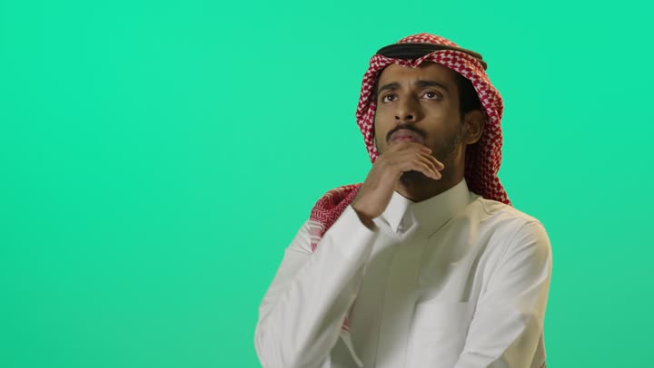لتأمل والتخطيط للمستقبل، التركيز وشرود الذهن والتمعن ، إيجاد حل لمشكلة ما،  بورترية مقرب لشاب عربي خليجي سعودي يرتدي الثوب الابيض و الشماغ يضع يده على ذقنه ينظر إلى الأعلى بإيماءات التفكير والتركيز، خلفية خضراء، كروما