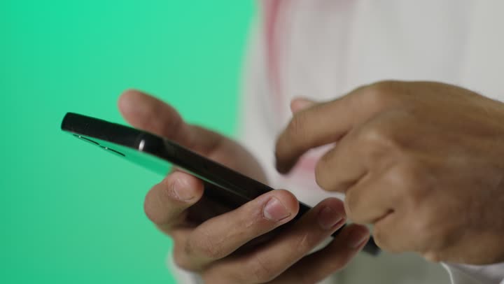 استخدام التقنية والتكنولوجيا والاجهزة الحديثة، تصفح مواقع التواصل الاجتماعي، بورترية مقرب لشاب عربي خليجي سعودي يقوم بالنقر على شاشة الهاتف المحمول، تصفح مواقع التواصل الاجتماعي، خلفية خضراء ، كروما