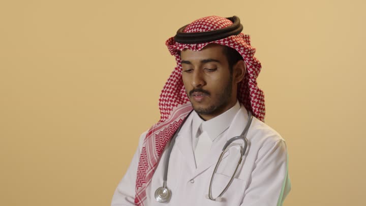 الاطلاع على نتائج الفحوصات،  تشخيص الحالات المرضية, بورتريه لطبيب عربي خليجي سعودي يرتدي الزي التقليدي والشماغ والمعطف الطبي يقوم  بإعداد التقارير الطبية, خلفية بيج