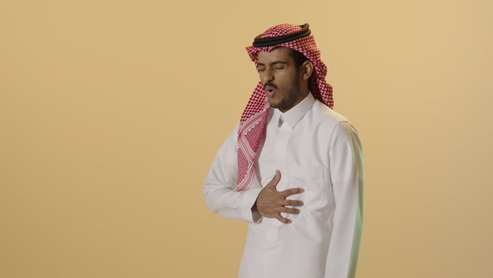 إيماءات وجه ويدين تدل على الوجع والألم، الحاجة إلى العلاج، بورترية لشاب عربي خليجي سعودي يرتدي الثوب الابيض و الشماغ  يعاني من آلام البطن والمعدة، مفهوم أمراض والتهابات الجهاز الهضمي، التعب والإرهاق والإحساس بالمرض، خلفية بيج