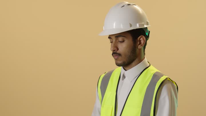 مخططات و مشاريع اعمارية، العمل في القطاع الهندسي، مهن ووظائف شبابية هندسية، بورتريه مقرب لمهندس عربي خليجي سعودي يرتدي الثوب الابيض والخوذة وسترة الحماية يحمل مخطط المشروع، الاشراف على العمل،  خلفية بيج
