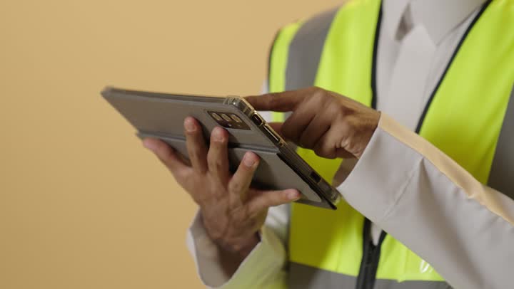 التأكد من سير الأعمال بالشكل المطلوب والصحيح، الأجهزة التقنية الحديثة، بورتريه مقرب ليد مهندس عربي خليجي سعودي يرتدي الثوب الابيض والخوذة وسترة الحماية باستخدام الجهاز اللوحي، تدوين و تسجيل الملاحظات, كتابة آخر المستجدات حول المشروع، خلفية بيج