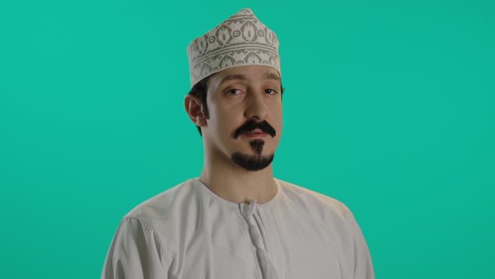 رجل عربي عماني خليجي يرتدي الكمة المطرزة و الدشداشة البيضاء يقف بثبات , رفع اصبع الابهام لاعلى اشارة الى الاعجاب و الرضا عن شئ ما , ايماءات وجه سعيدة و فرحة , تصوير مقرب