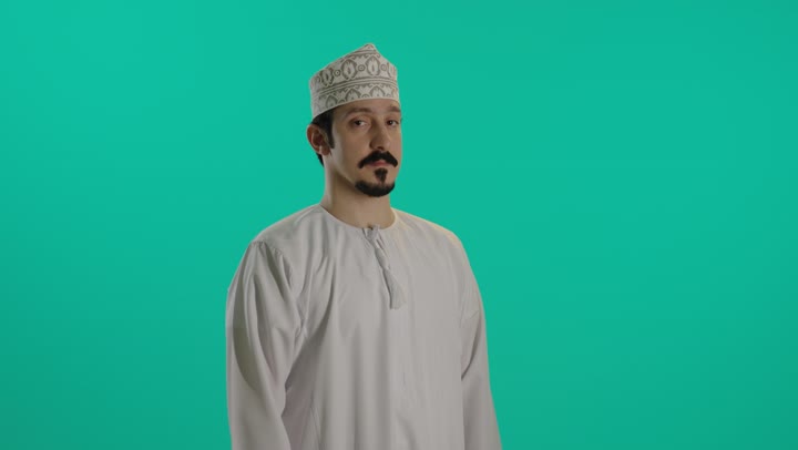 شاب عربي خليجي عماني يرتدي دشداشة بيضاءو كمة مطرزة يشير باصبع الابهام لاسفل اشارة الى عدم الاعجاب بشئ ما , تعابير وجه محبطة, ملامح الاستياء و الغضب