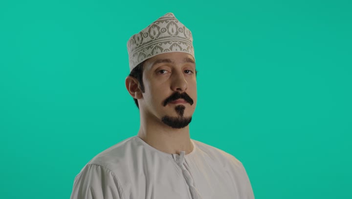 الوقوف امام الكاميرا في غضب مع رفع الذراع و فتح الكف اشارة الى التوقف , رجل عربي خليجي عماني يرتدي دشداشة بيضاء و كمة مطرزة يفتح قبضة اليد علامة على منع التقدم اكثر , ممنوع الاقتراب