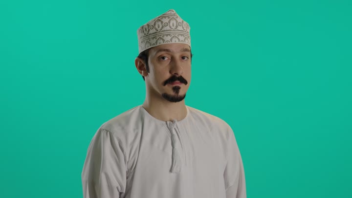 وضع اصبع السبابة على الفم اشارة الى التوقف عن الكلام , رجل عربي خليجي عماني يرتدي الدشداشة البيضاء و كمة مطرزة , ايماءات الاستياء و الغضب