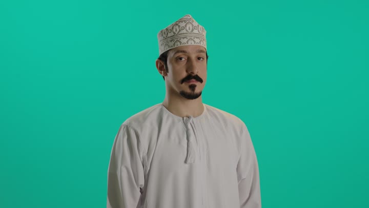 رجل عربي خليجي عماني يرتدي دشداشة بيضاء و الكمة المطرزة يحرك اليد اشارة لطلب الاتصال الهاتفي , رفع الخنصر و الابهام و اغلاق الاصابع الباقية , اشارة شاكا , ايماءات السعادة و الفرحة