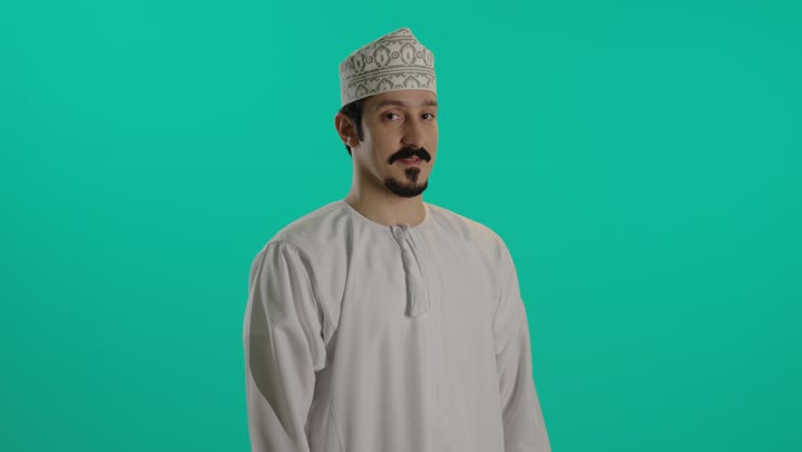 Expressions of happiness are clear when achieving victory and successfully completing tasks. An Arab Gulf Omani man wearing a white dishdasha and an embroidered kumma raises his fists in the air as a sign of enthusiasm and cheering. There is a smile and joy upon achieving victory.